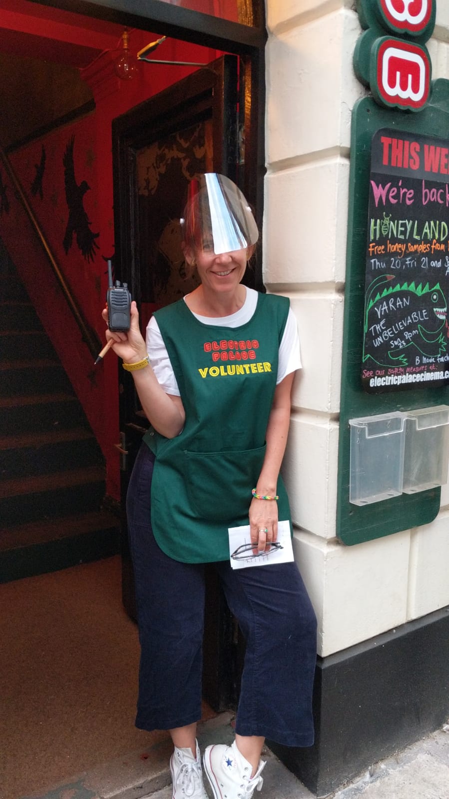 Woman in cinema doorway holding payment machine in hand and smiling